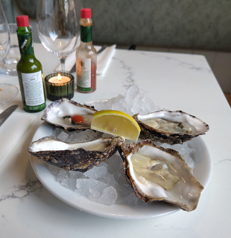 Four oysters on a place with ice, with a slice of lemon.